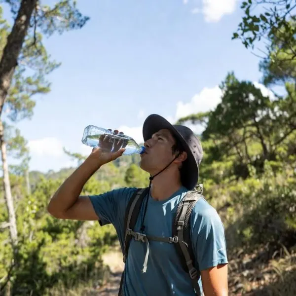Jovem que está a caminhar em trilhos faz uma paragem para beber água e manter-se hidratado.